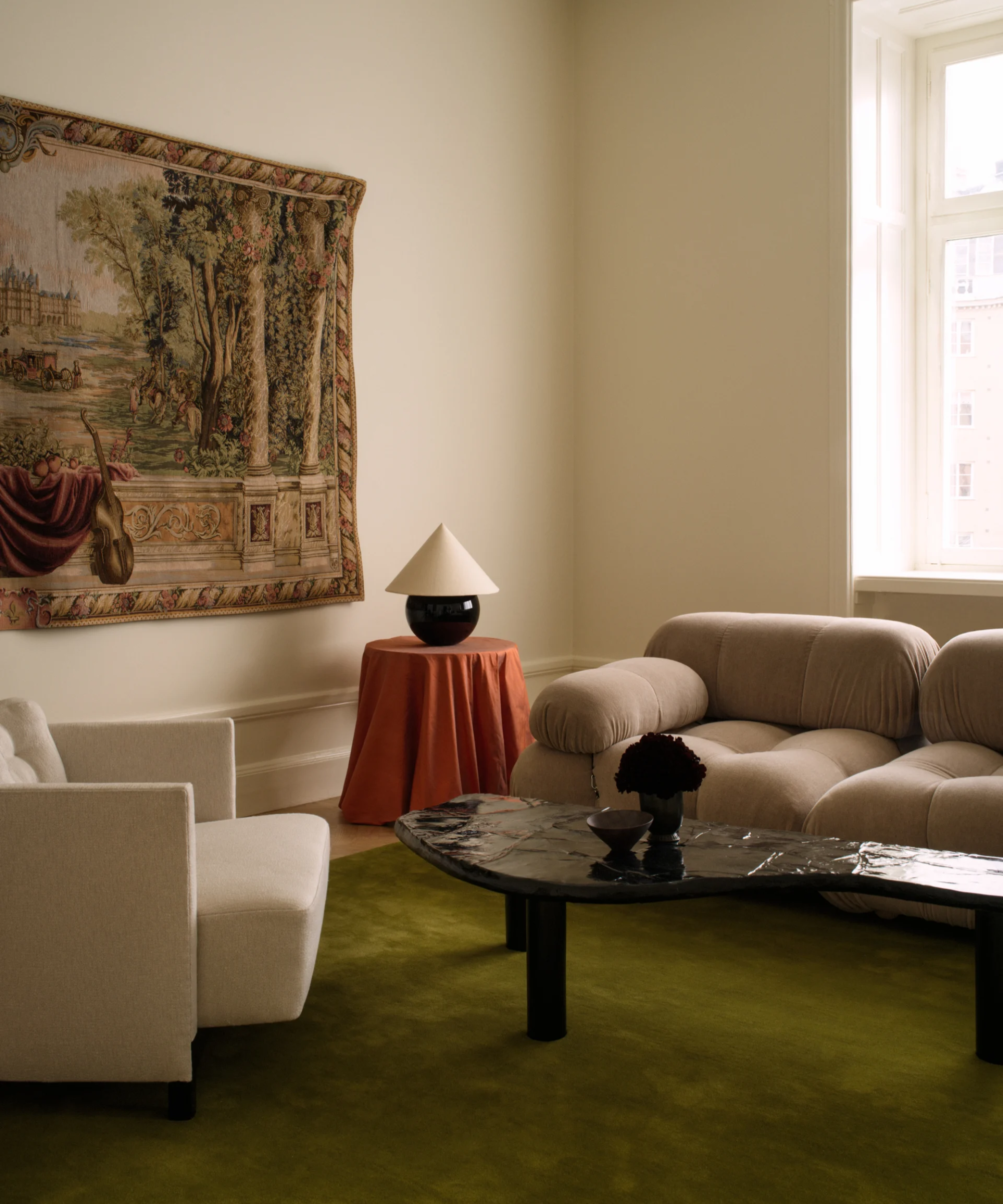 Moss green rug anchoring a living room styled with contemporary low-slung furniture and an antique tapestry wall hanging.