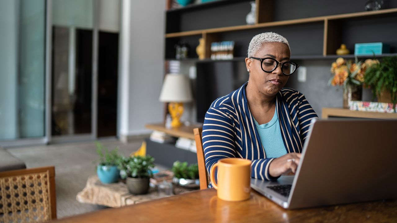 An older woman works on her laptop in her living room.