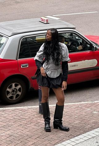 an influencer's outfit with a black mini bubble skirt styled with knee-high moto boots and a baggy gray t-shirt