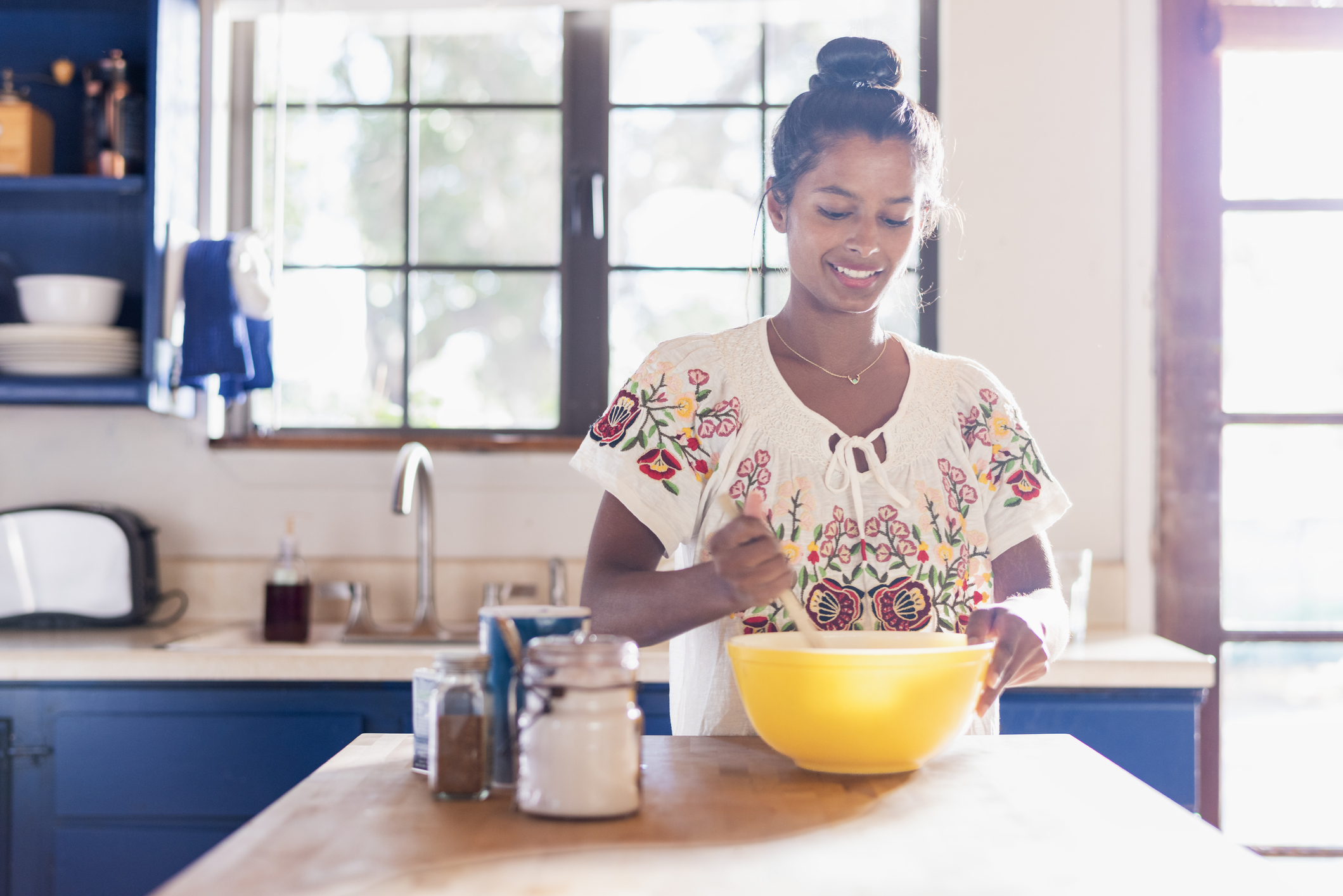 Woman in a kitchen using a wooden spoon to stir something in a yellow mixing bowl