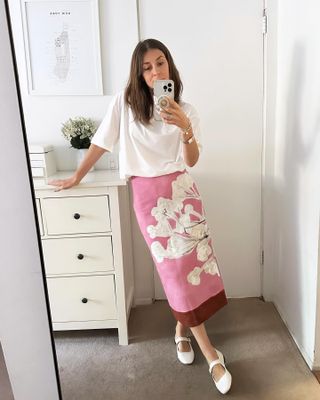 Woman wearing white T-shirt, pink skirt, and white Mary Janes.