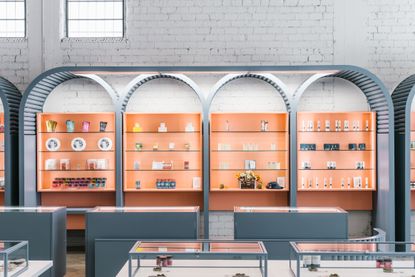 Green Qween Marijuana dispensary dispensary, Los Angeles. Grey counters with glass tops in front of an orange wall with shelves which are curved on the tops.