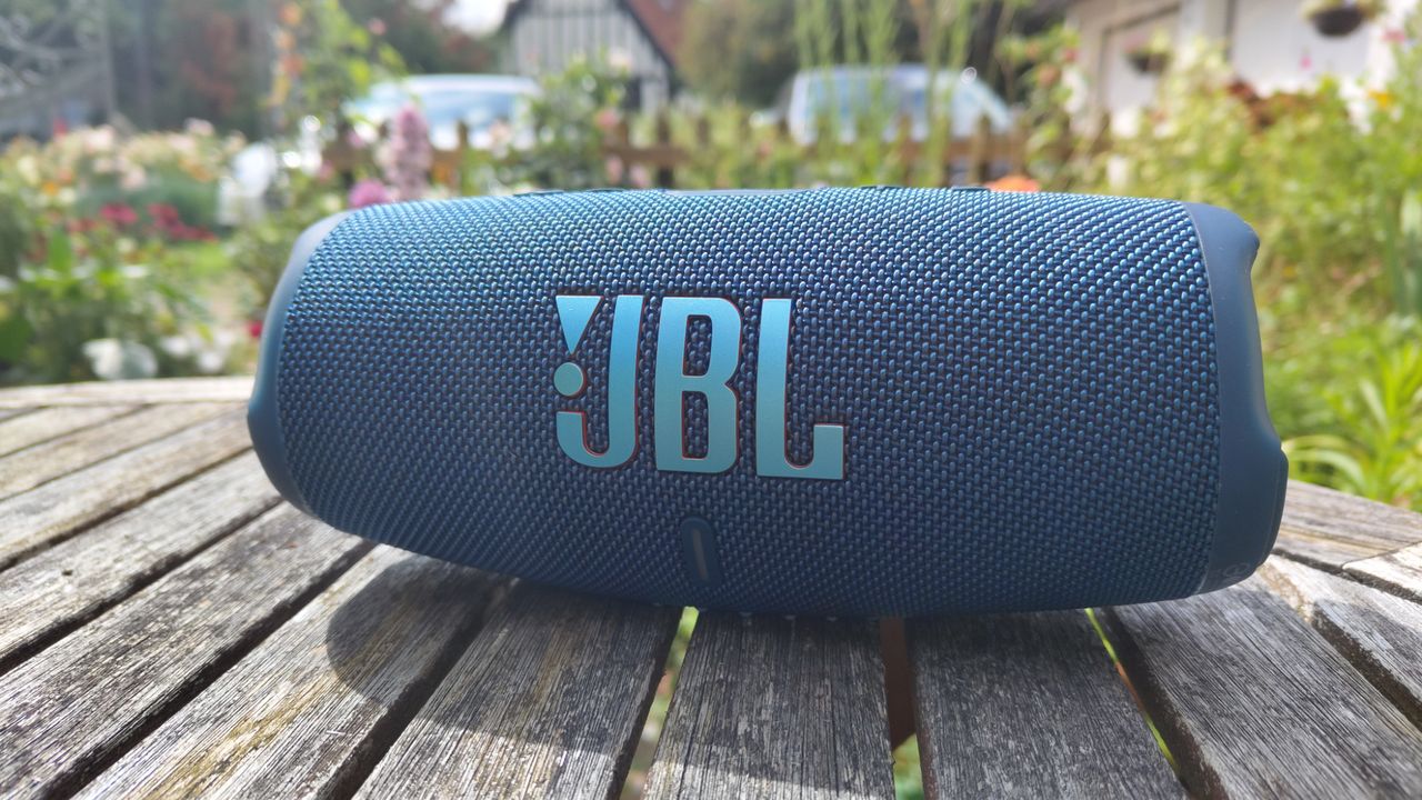 A black JBL Charge 5 on a wooden garden table.