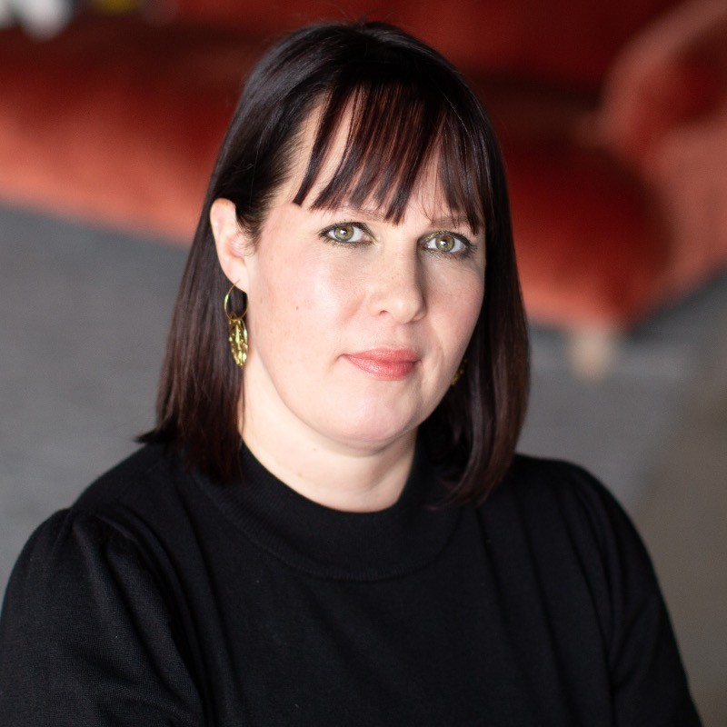 A woman with a black bob and fringe wearing a black top and gold earrings and smiling at the camera