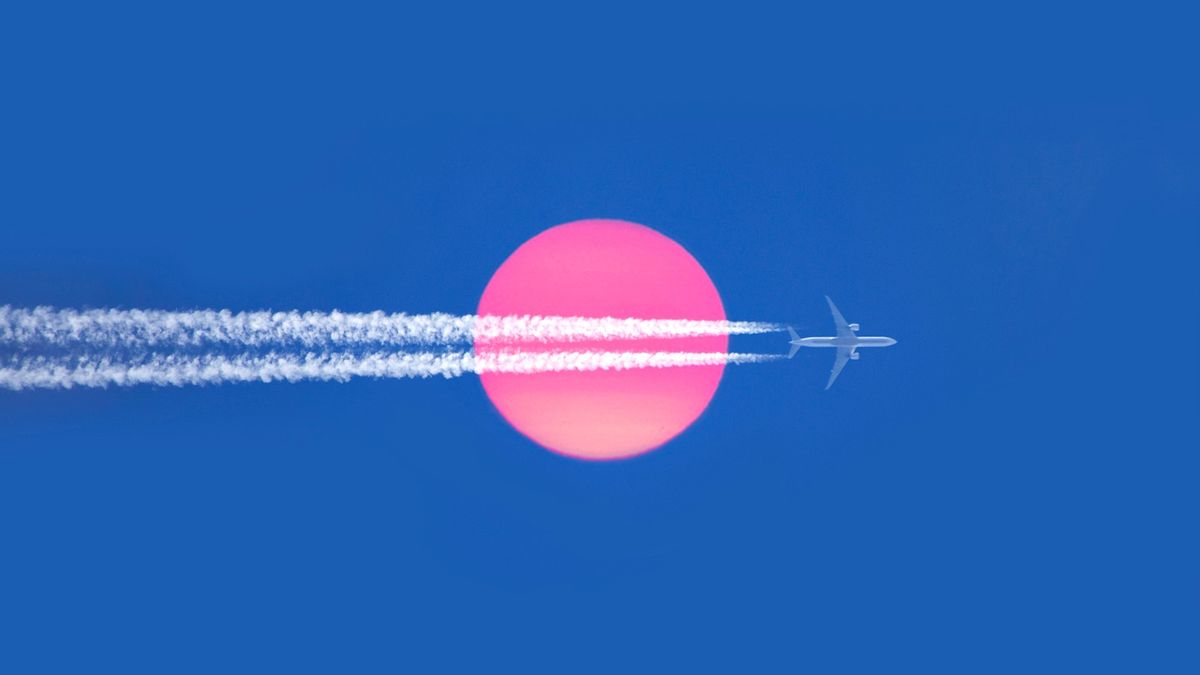 An airplane with contrails across the surface of a pink hued sun against a blue sky.