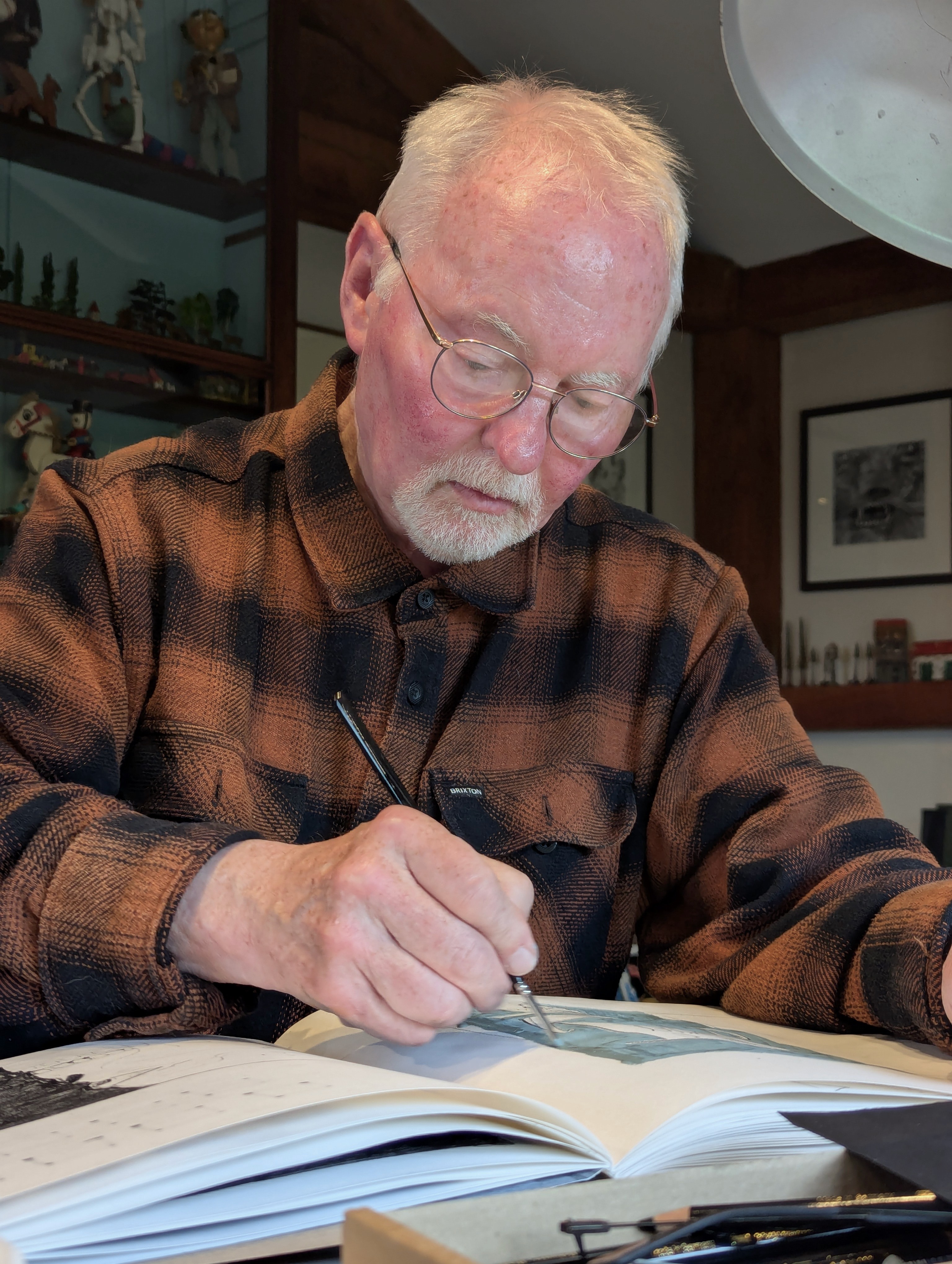 Clive Hicks-Jenkins, dressed in a brown check shirt, sketching in a book