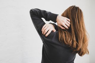 PMS symptoms: Rear view of a woman holding her shoulder because of shoulder pain