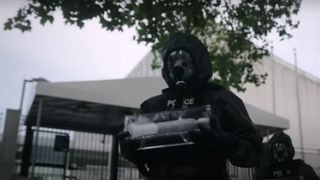 Two police officers wearing gasmasks and holding a glass box during The Night Agent season 2