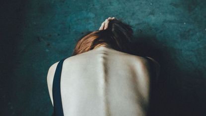 Woman doubled over forwards holding her hair up as seen from behind.