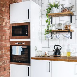 Kitchen with a white tiled and an exposed brick wall, white wall and floor units and patterned ceramic tiled floor