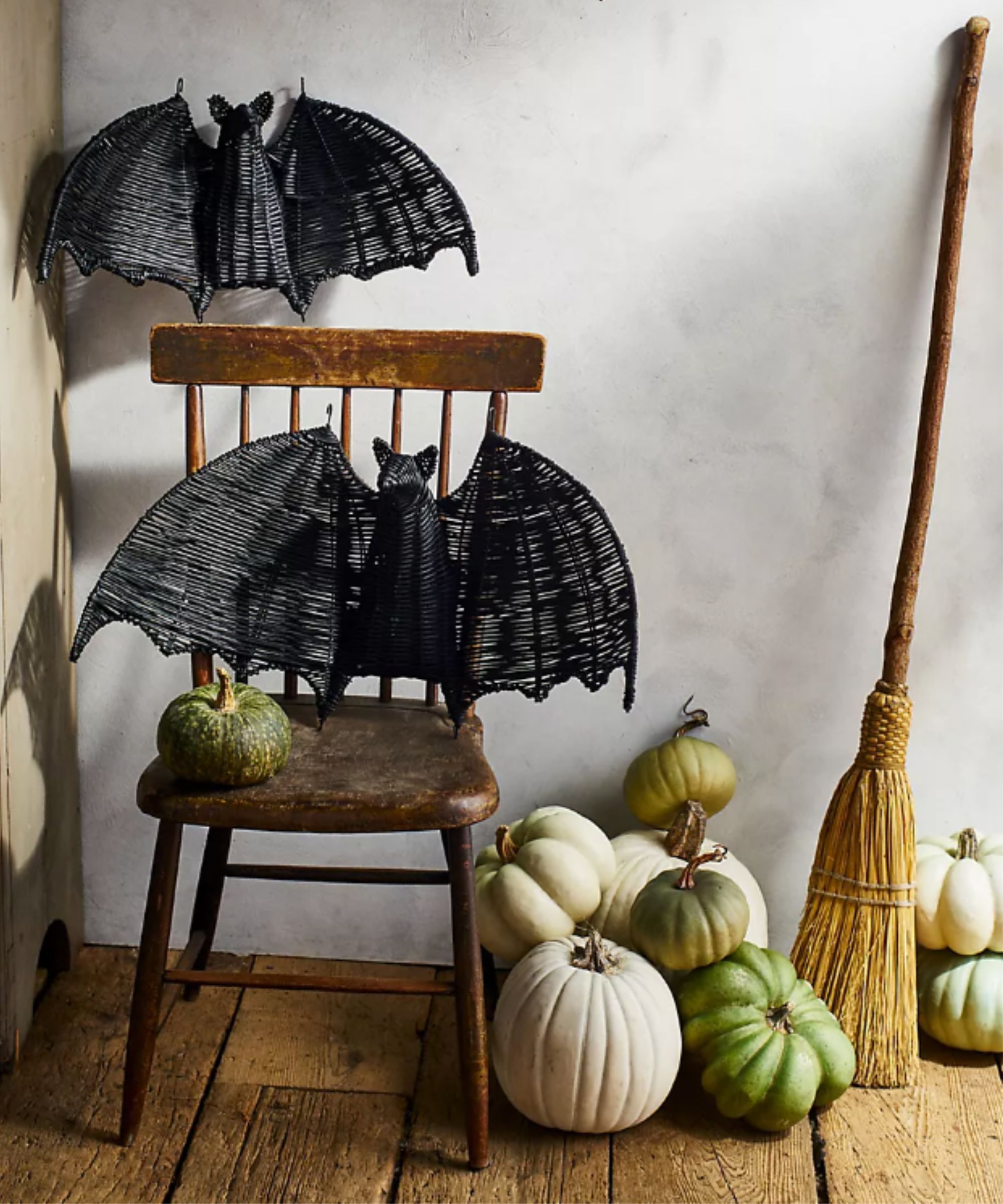 Black rattan bat decorations on a wooden chair with white and green pumpkins and a broomstick