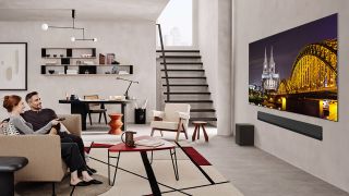 Two people watching the LG G5 TV, which is mounted on a wall in a spacious living room