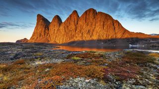 sunrise at scoresby sund shows a large rocky mountain outcrop bathed in golden light.