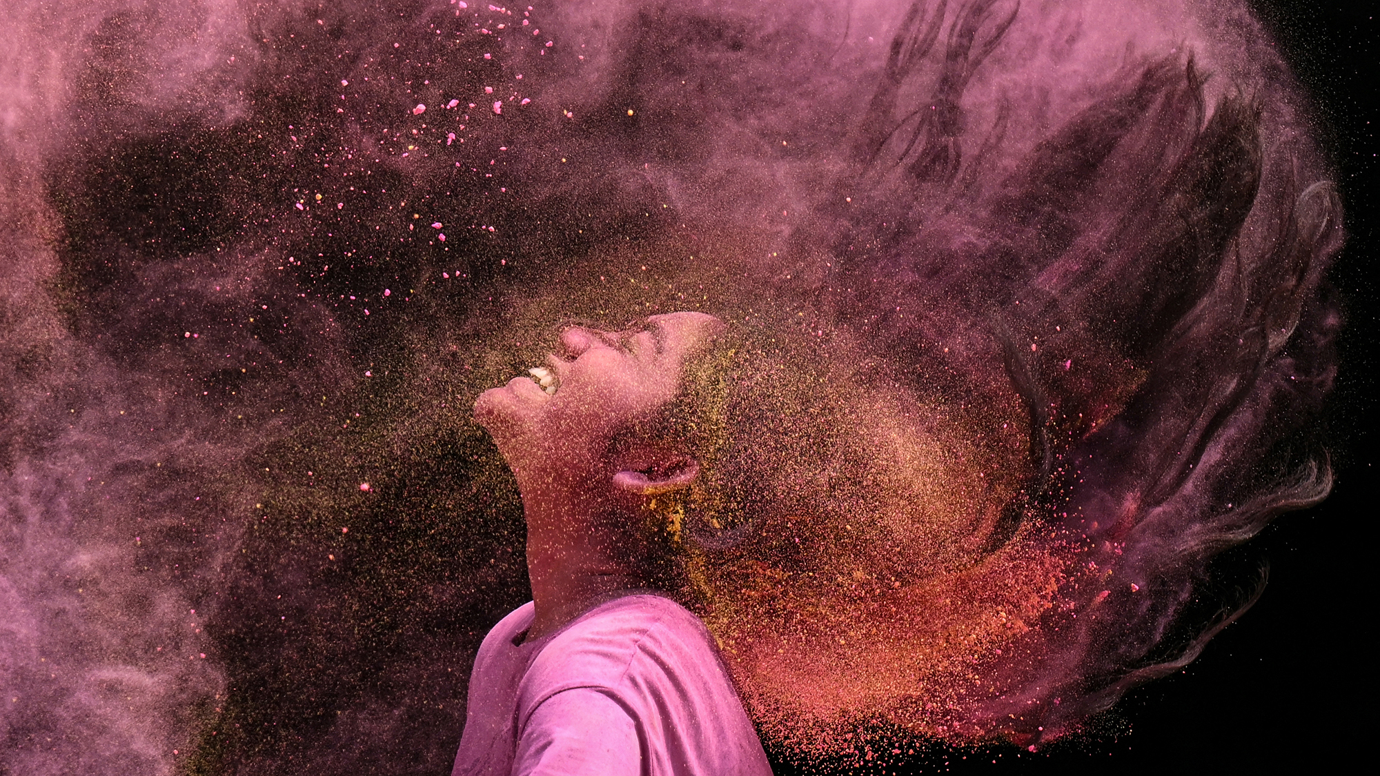 A woman tosses her hair in a cloud of colored powder during the Hindu festival of Holi in Chennai, India