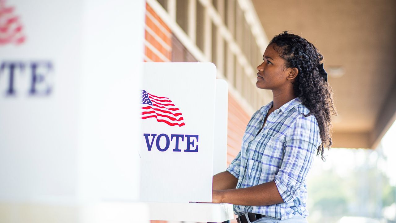 Young girl standing in front of a voting booth on election day, looking thoughtful