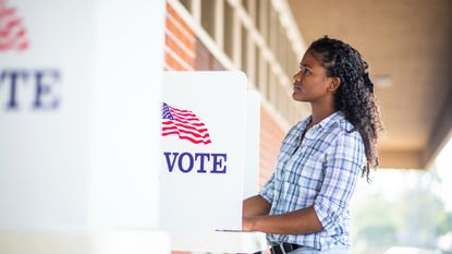 Young girl standing in front of a voting booth on election day, looking thoughtful