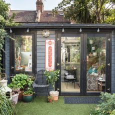 Garden room summer house painted black with wood panelling, festoon lights and pot plants