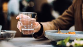 Is fasting good for you? Image shows person holding a glass of water and a bowl of food