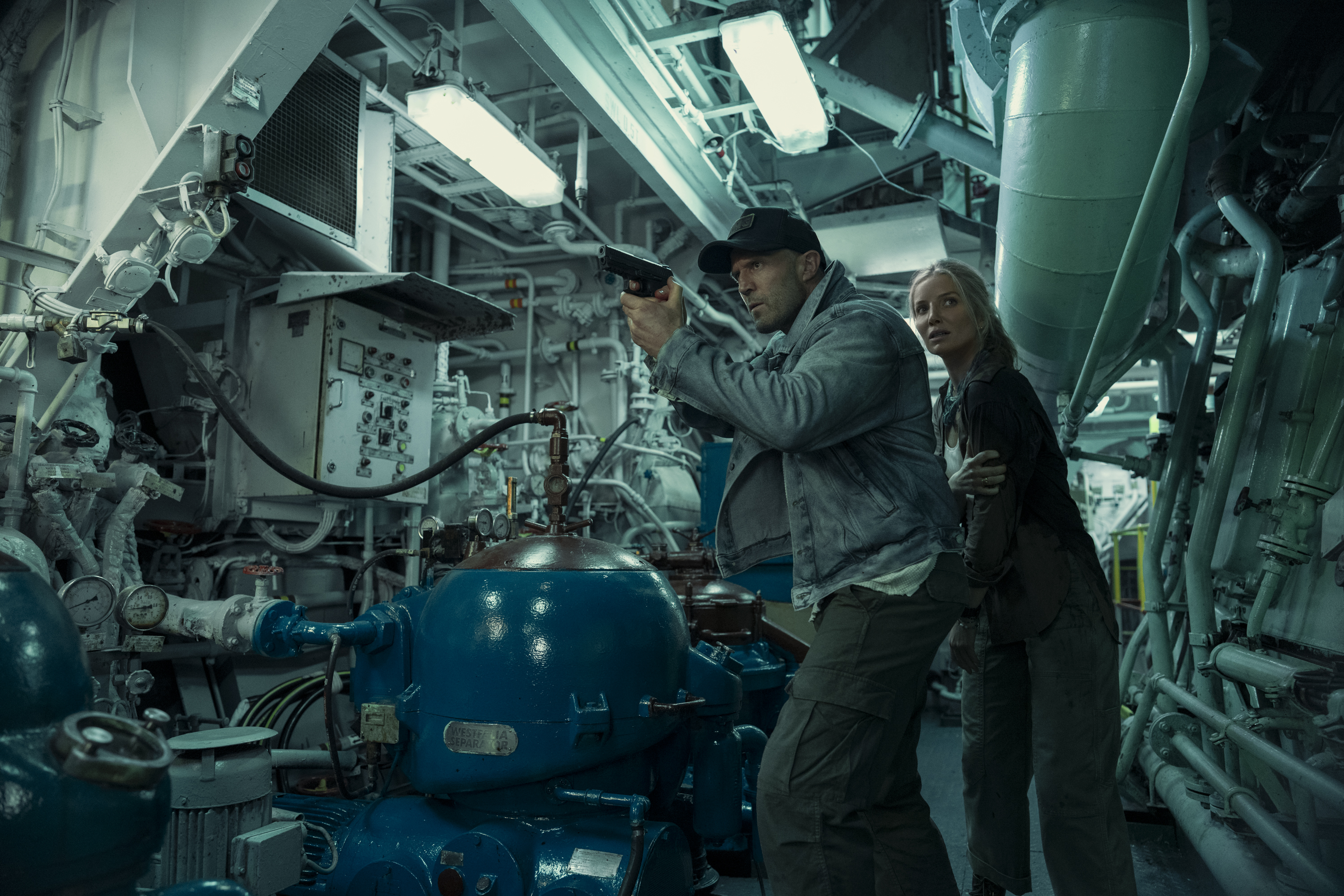 Jason Statham as Cole Reed and Annabelle Wallis as Angie Ellis walking through the dark mechanical room of a facility pointing a gun in a still from the action movie mutiny