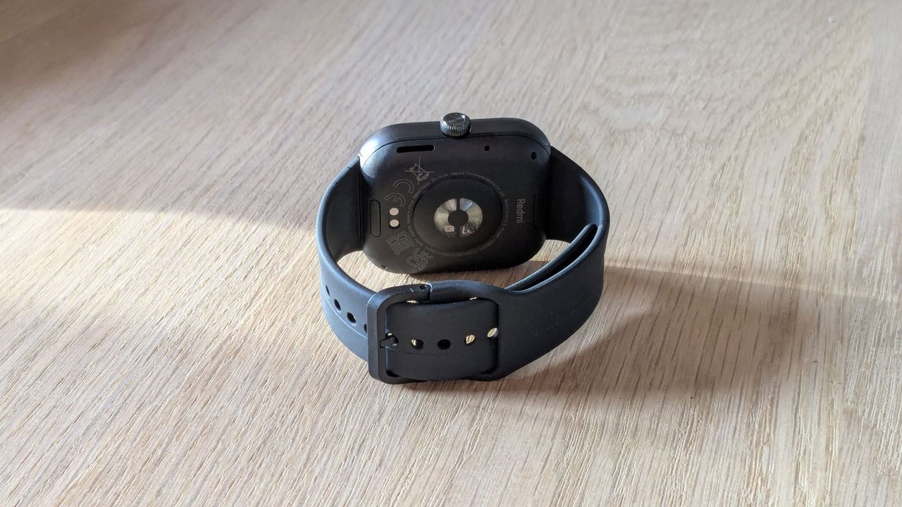 The Redmi Watch 5 showing the tucked in strap on wooden table.