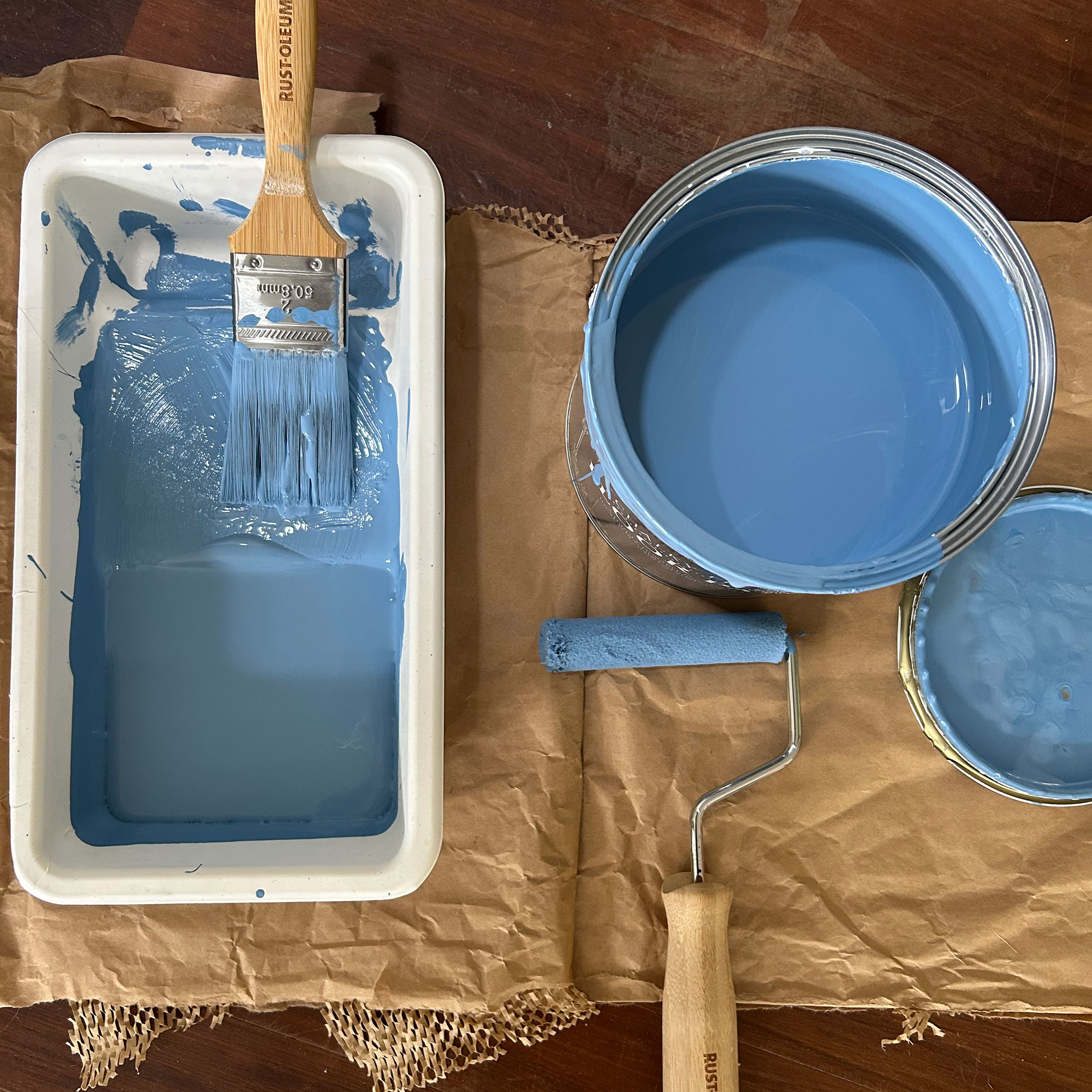 Open tin of blue paint beside used roller and pan with paintbrush