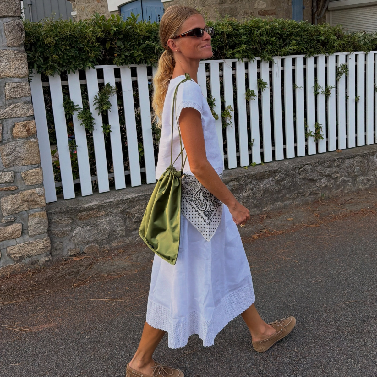 Influencer Alice Pilate wearing a white dress and green satin pouch bag. 