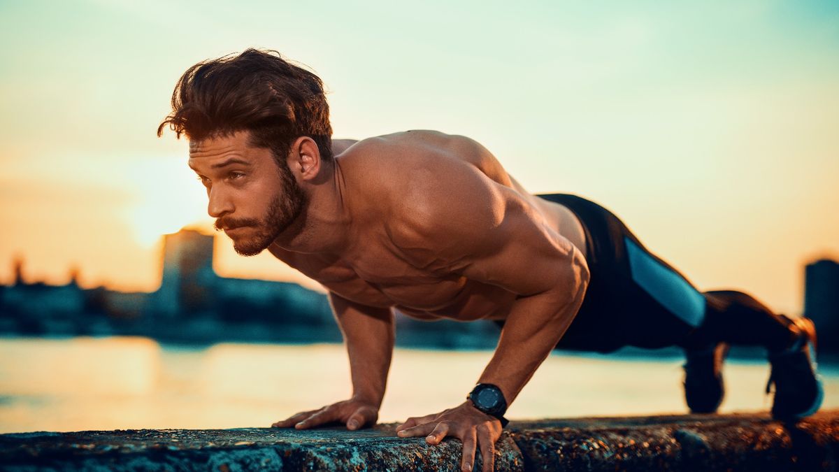 Man outdoors performing a press up on a wall against a backdrop of water performing compound exercise