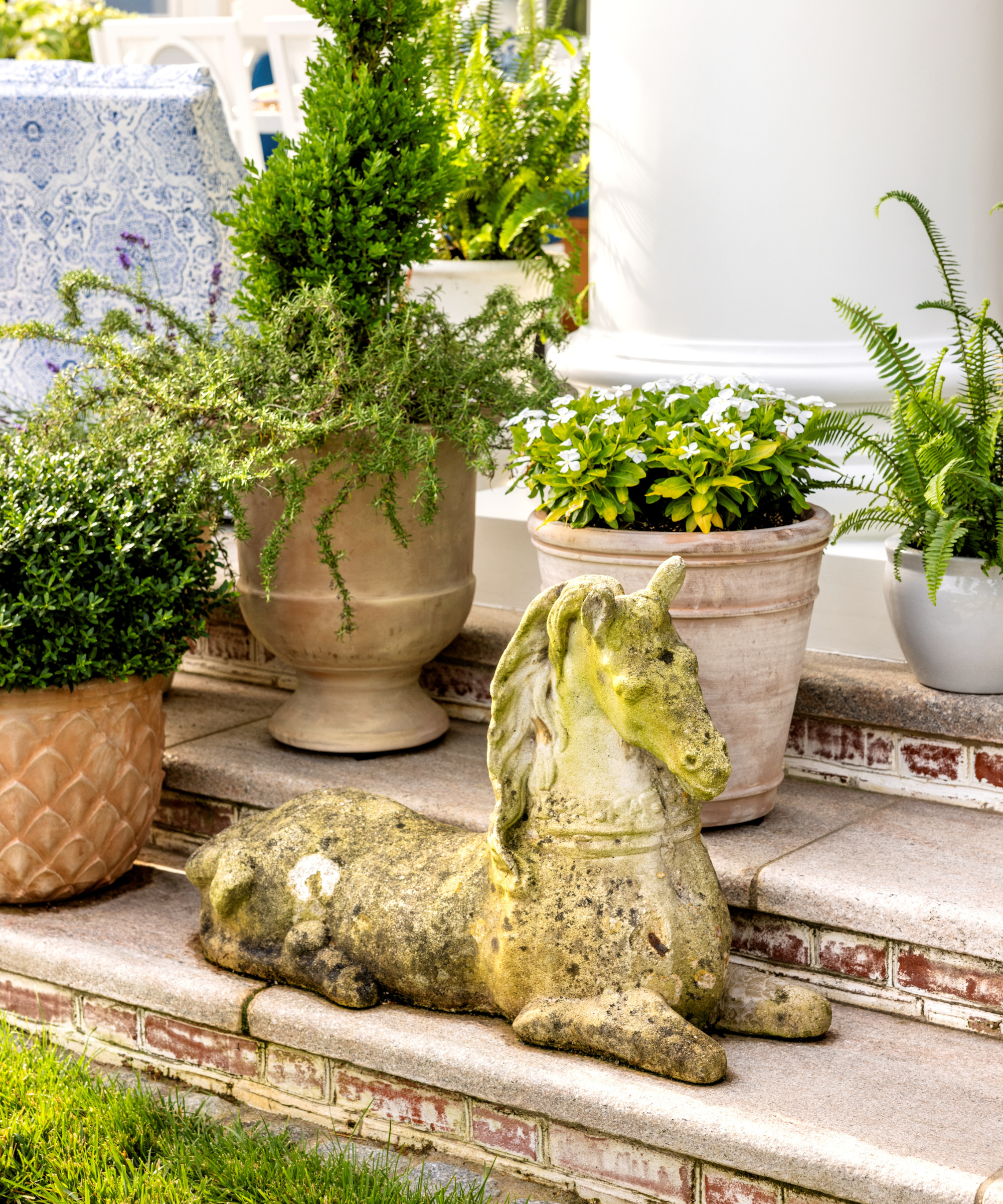Colonial Revival back patio featuring a stone horse statue sitting on a set of steps, surrounded by several planters.
