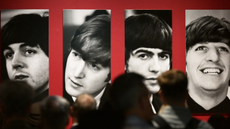 People stand in front of four black and white portraits, one of each of the members of The Beatles