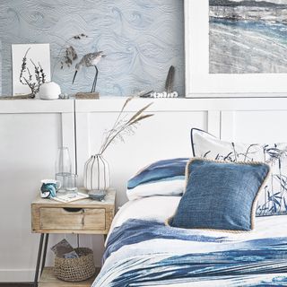 coastal bedroom with nautical theme, blue and white bedding, wave wallpaper, artwork, nautical accessories, weathered bedside