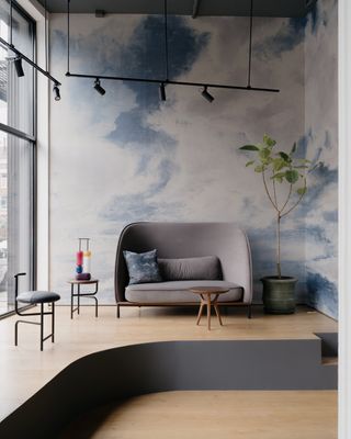 Wallpaper with clouds with furniture display including small grey sofa