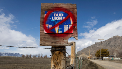A signpost with a Bud Light post has a red circle and cross spraypainted over it