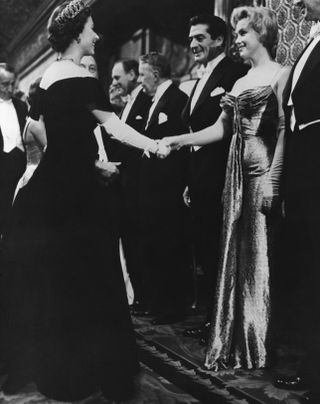 Queen Elizabeth II of England offers a gloved hand to Hollywood glamour girl Marilyn Monroe Miller during the Queen's visit with celebrities at the Royal Film Performance. Standing beside Marilyn is actor Victor Mature.