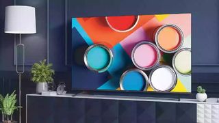 The 55-inch version of the Hisense A6G stands on a TV table, displaying different coloured paint cans. 