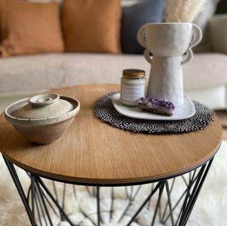 Small round wooden coffee table styled with unique vase and small pot