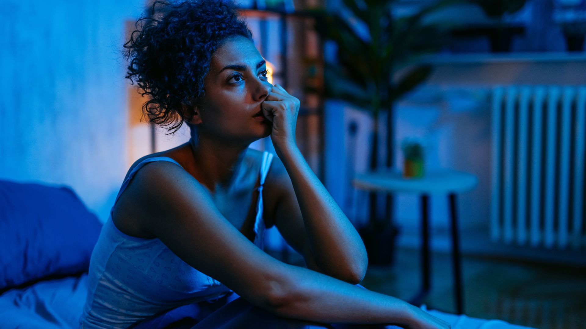A woman sits up in bed at night looking unhappy as she is unable to sleep.