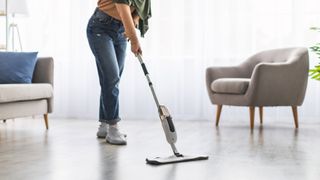 Woman cleaning living room floor with a steam mop.