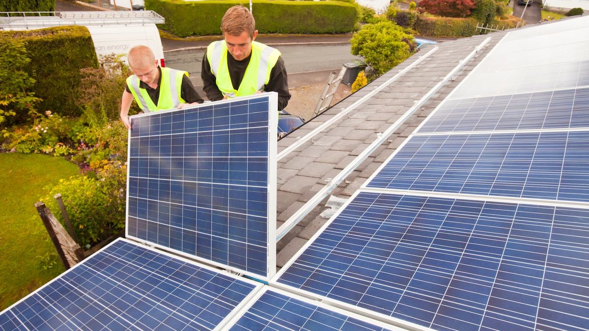 Technicians fitting solar photo voltaic panels to a house roof in Ambleside, Cumbria, UK.