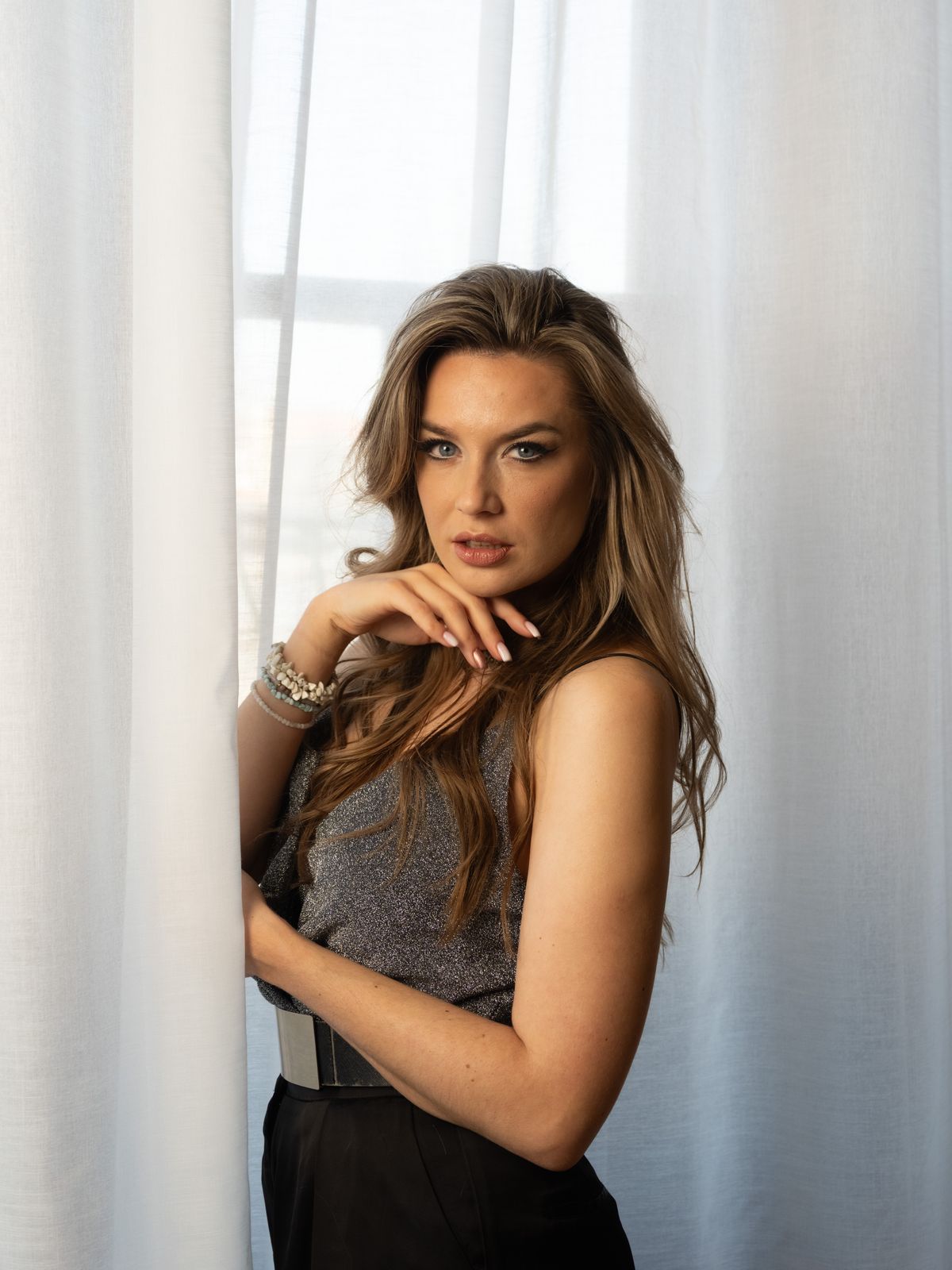 Person posing in front of white drapes covering a window