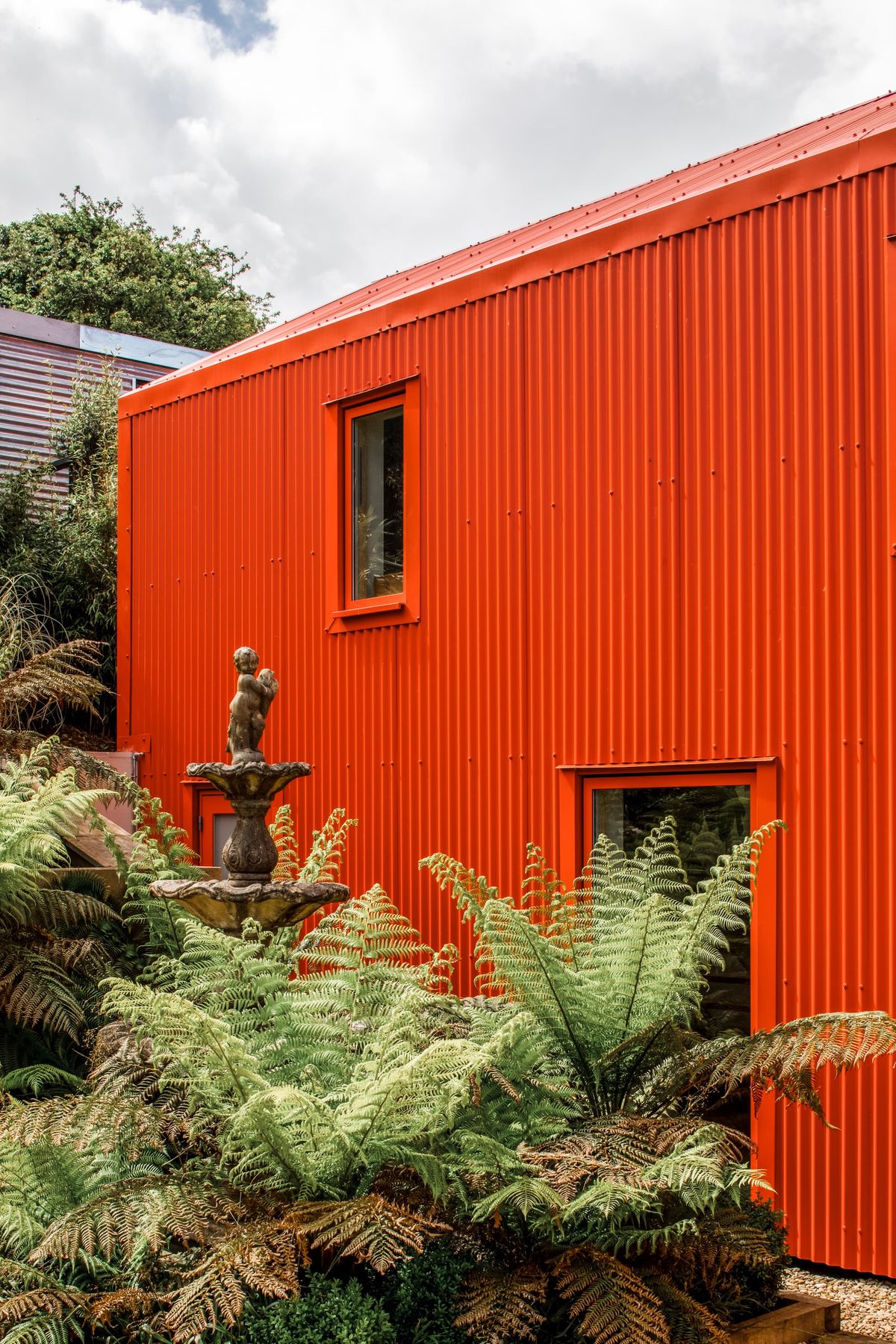 A modern home extension clad in bright orange metal with a water fountain