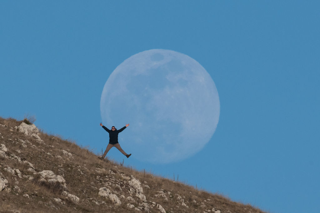 Una persona allarga le braccia e le gambe davanti alla luna piena