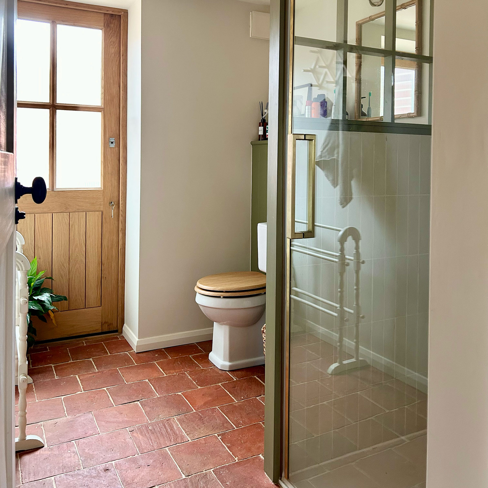 Bathroom with terracotta floor, wooden external door, glass-fronted shower inclusion and loo with wooden seat