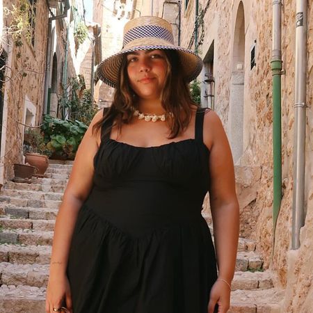 Woman wearing plus-size fashion dress black corset mini dress standing in European-style alleyway.