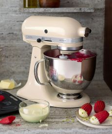 A cream KitchenAid stand mixer surrounded by red velvet madeleines and pistachio cream. 