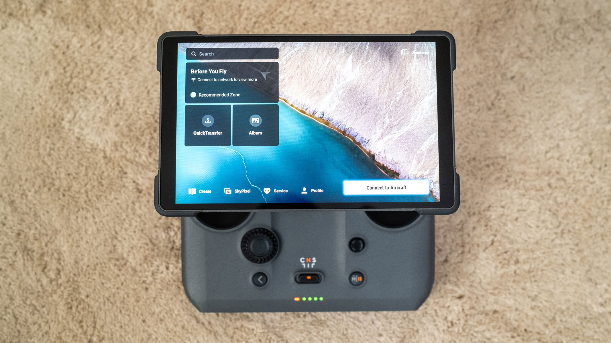 A bird's eye view of a grey controller has a screen attached which looks larger than the controller itself, is on a beige carpet.