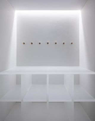 A brightly lit cloakroom area with white walls, white cubby holes and coat pegs.