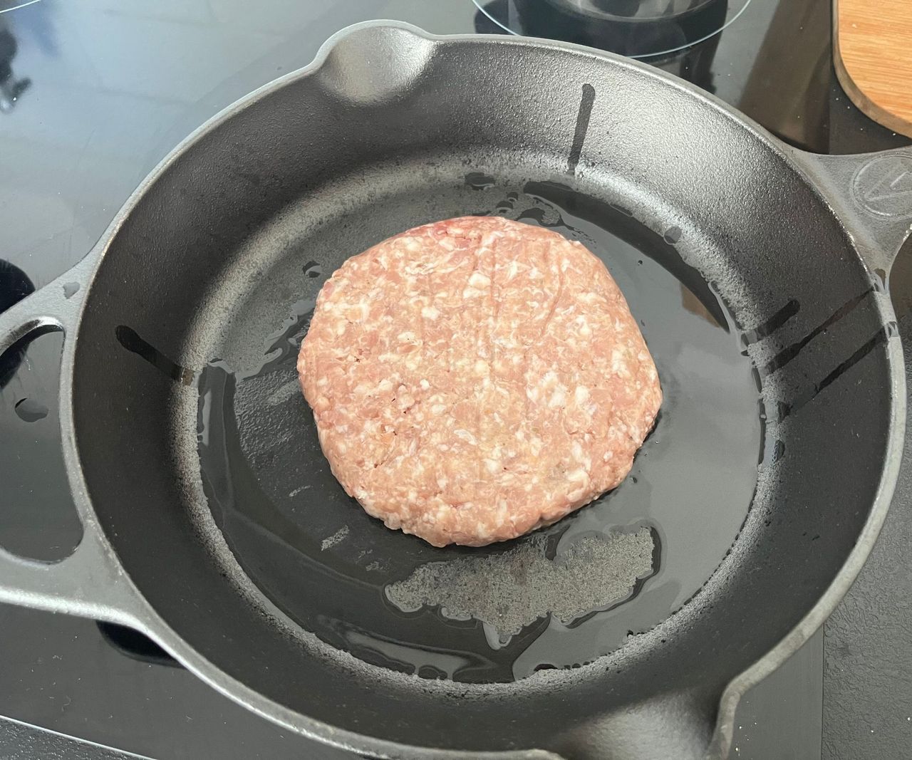 A small black cast-iron skillet on a black stove with a raw burger inside