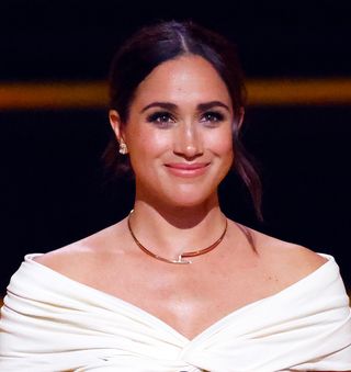 Meghan Markle smiling at the camera in a white off the shoulder top