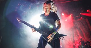 Greg Mackintosh of Paradise Lost plays his custom 7-string V live onstage with red and white stagelights behind him.