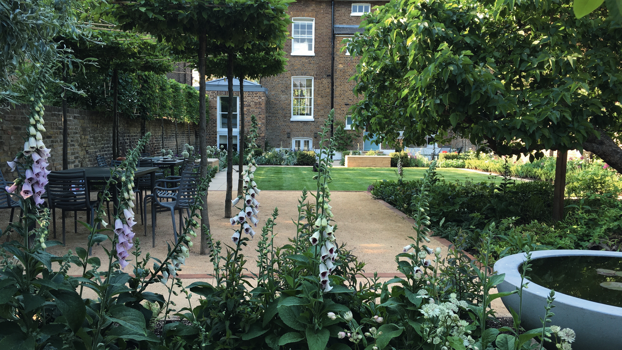 large garden with pergola over seating area, paving, lawn and lots of planting